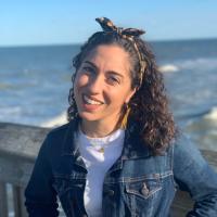 Tina stands on the pier at the beach, smiling.