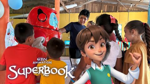 Chris from Superbook stands in the foreground on the right side of the photo, smiling and pointing back toward a group of children in Costa Rica meeting Gizmo for the first time. The CBN Animation and Superbook logos are stacked in the bottom left corner of the photo.